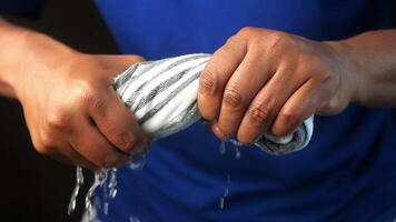 slow motion of Hands squeeze wet towel against black background. draining water from wet towel.. video