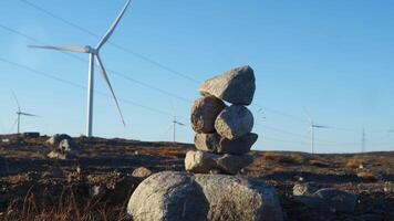 wind turbines are located in tundra of Nordic country, generating electricity. In background, pebbles are stacked on top of each other, indicating direction of hiking trail. video