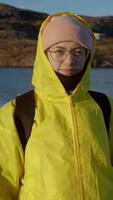 Portrait of beautiful young woman, warmly dressed in bright yellow raincoat with hood, in northern landscape with cold sea in background. video