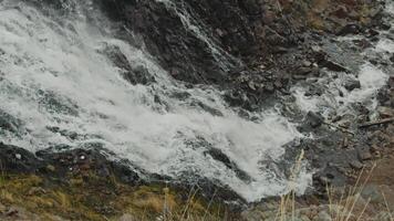 A waterfall with a powerful stream of cold water flows over large rocks in the midst of the northern tundra. video