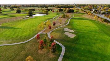Aerial View of Scenic Golf Course in Autumn. Expansive golf course with lush green fairways, sand bunkers, winding paths, and colorful autumn trees under a sunny sky. video