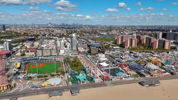 New York State, US. 10.11.2024 Aerial View of Amusement Park and Cityscape. Expansive aerial view of a beachfront amusement park, baseball stadium, and urban skyline under a bright blue sky with video