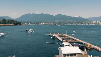 Vancouver Canada 20.09.2024 Seaplanes docked at harbor with mountainous backdrop. Seaplanes are docked at a waterfront harbor, with a stunning backdrop of mountains and a city skyline. video