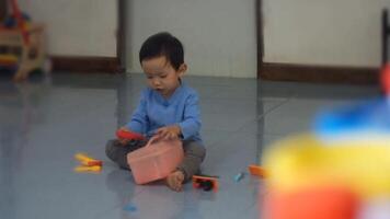 An Asian toddler is sitting and playing with a plastic toolbox on a tiled floor. video