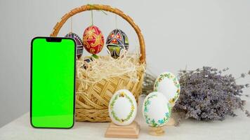 Basket smartphone eggs and a green screen phone on a white background. Chroma key vertical smartphone mock up for advertising on the eve for the Christian holiday video