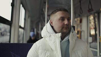 Male passenger in casual winter in tram or a bus, he is looking through a window and using a smart phone video