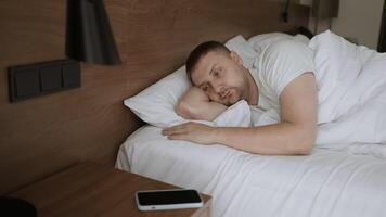 Handsome sleepy Caucasian man is sleeping in the bed, he wake up for looking how time on smartphone video
