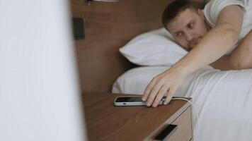 Smartphone Alarm Clock App. Handsome Caucasian man sleeping on the bed awakening by smartphone alarm clock ringing news. video