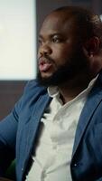 Vertical African american agent and his colleague analyzing evidence in a lounge, emphasizing strategic thinking and teamwork to accomplish a surveillance mission. Reading critical documents. Camera B. video