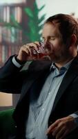 Vertical Old money elite gentleman drinking strong whiskey due to stress in a luxurious classy lounge, being dizzy with a headache. High society member getting tipsy, day drinking. Camera B. video