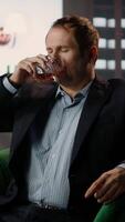 Vertical Old money elite gentleman drinking strong whiskey due to stress in a luxurious classy lounge, being dizzy with a headache. High society member getting tipsy, day drinking. Camera A. video
