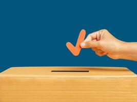 Hand holding a red check mark symbol overhead the voting box at place election with a blue background photo