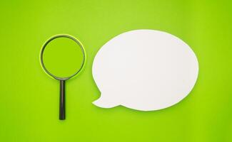 Top view of a blank white speech bubble and a magnifying glass isolated on a light green background photo