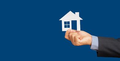 Hand businessman holding a house mockup paper while standing on a blue background photo