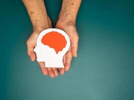 Top view of head with a brain made from paper on the palm senior woman over a green background photo