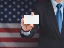 The businessman's hand shows a blank business card while standing on the American flag background photo