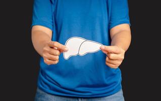 Hands holding a liver shape symbol made of paper while standing on a black background photo
