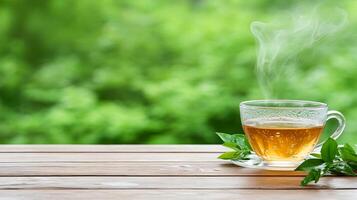 Steaming green tea in a glass cup on a wooden table with leafy green background photo