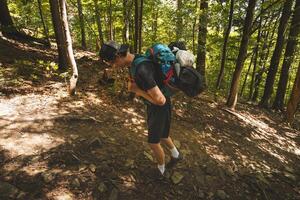Hiker trekking uphill through a dense forest, carrying a loaded backpack on a rugged path. A moment of resilience, strength, and connection with nature challenges photo