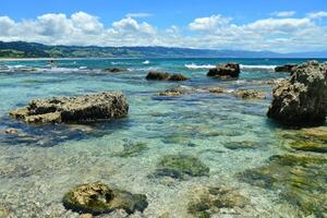 A serene coastal landscape with clear waters, rocks, and a blue sky. photo