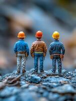 Three miniature construction workers facing away, set against a blurred rocky background. photo
