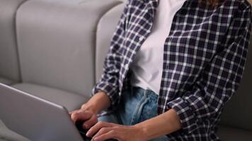 Smiling Caucasian woman on couch using laptop typing message happy lady girl female freelancer client chatting computer browsing surfing internet social media studying working online remote at home video