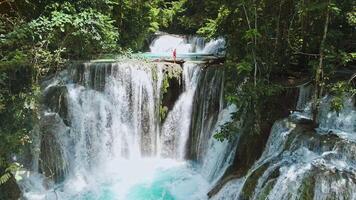 Powerful cascade waterfalls and a woman stands on a rock and admires the landscape, drone view video