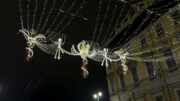 Intricately designed Christmas decorations with illuminated crowns and angelic figures hang above a historic street in Saint Petersburg. Strings of fairy lights create a magical canopy, enhancing the video