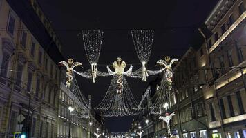 Intricately designed Christmas decorations with illuminated crowns and angelic figures hang above a historic street in Saint Petersburg. Strings of fairy lights create a magical canopy, enhancing the video