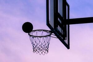 Silhouette of a Basketball and Hoop Against a Vibrant Evening Sky Capturing the Essence of Outdoor Sports and Recreation photo