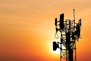 Silhouette of a Communication Tower Against a Vibrant Orange Sunset Sky with Antennas and Cables in a Scenic Evening Landscape photo