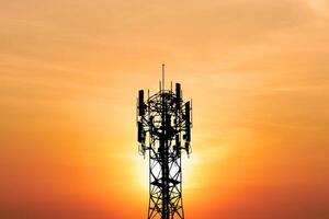 Silhouette of a Communication Tower Against a Vibrant Orange Sunset Sky with Radiant Sunlight in the Background photo