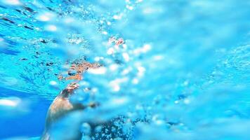 Man smiling on camera underwater in the pool. Happy man dives under the blue clear water and swimming inside the swimming pool in summer. video