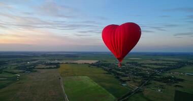 Red airship in the shape of a heart. Hot air balloon in the sky over a field in the countryside flying in the beautiful evening sky. video