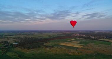 Red air balloon in love heart shape. Panoramic view on nature landscape and beautiful hot air balloon. Bright aerostat flying over the fields. video