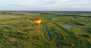 Colorful aerostat. Beautiful hot air balloon travels in the air on the background of green fields and small lakes in the rural place. Aerial view. video