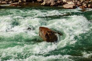 a large stone lies in the middle of a mountain river, the river flows and goes around the stones. Creation of river foam photo