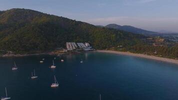 Aerial view of a lively beach on Phuket Island, Thailand, with turquoise waters, a resort near the shore, and lush green hills in the background. video