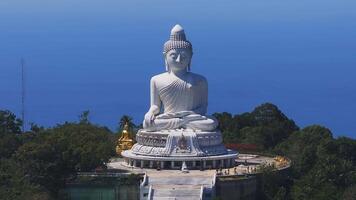 Aerial view of the Big Buddha statue in Phuket, Thailand, seated on a green hill with ocean in the background and dense vegetation surrounding it. video