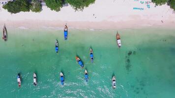 Aerial view of a pristine beach on Phi Phi Island, Thailand, featuring turquoise waters, long tail boats, lush greenery, and scattered beachgoers. video