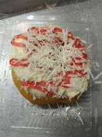 Closeup of a fried donut topped with butter, shaved cheese and strawberry jam photo