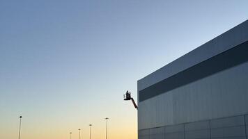Worker on Lift Maintaining Exterior of Modern Building at Dusk photo
