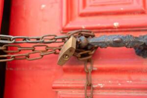 Closeup of metallic chains and locks in handles on red closed doors photo