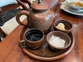 Traditional Clay Teapot Set with Sweeteners on Wooden Table in Restaurant Setting photo