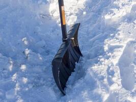 Black snow shovel clearing heavy snow from snowy path ensuring safe access and clean walkway. Focus on black snow shovel moving fresh snow maintaining clear paths and outdoor spaces efficiently photo