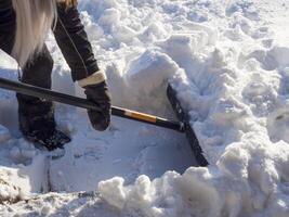 Person in winter attire shoveling snow on bright sunny day, clearing snow from path or driveway with care. Surrounded by snow, they enjoy crisp cold air while ensuring safe access. photo