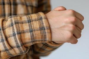 man holds his wrist pained expression while wearing plaid shirt. focus hand and wrist area white backdrop highlighting discomfort associated wrist strain photo