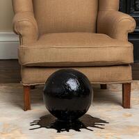 Black sphere with drips on carpet in front of armchair photo