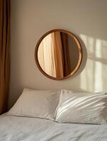 Sunlight streams through linen curtains onto a cozy bed with white pillows and a round wooden mirror photo
