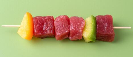 Delicious tuna and fruit skewers on a green background photo